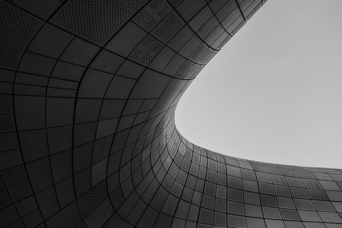 Curved, futuristic building facade in black and white, with sleek, geometric panels reminiscent of a Kubernetes cluster design and a gap opening to the sky.
